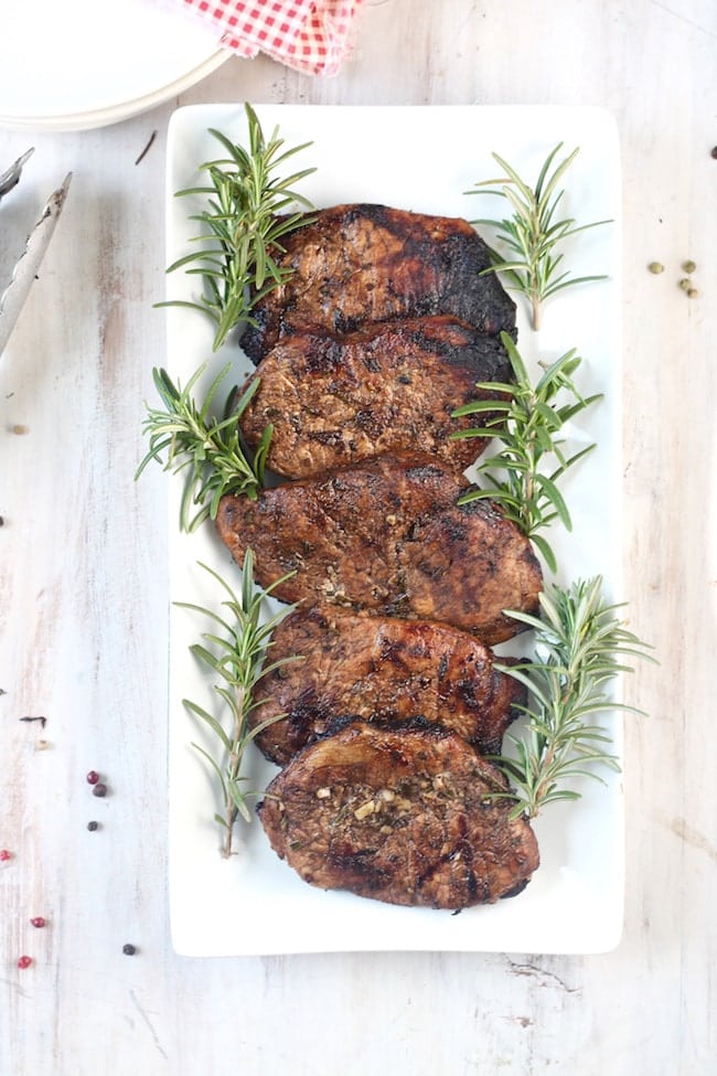 5 grilled balsamic pork chops garnished with fresh rosemary on a white platter