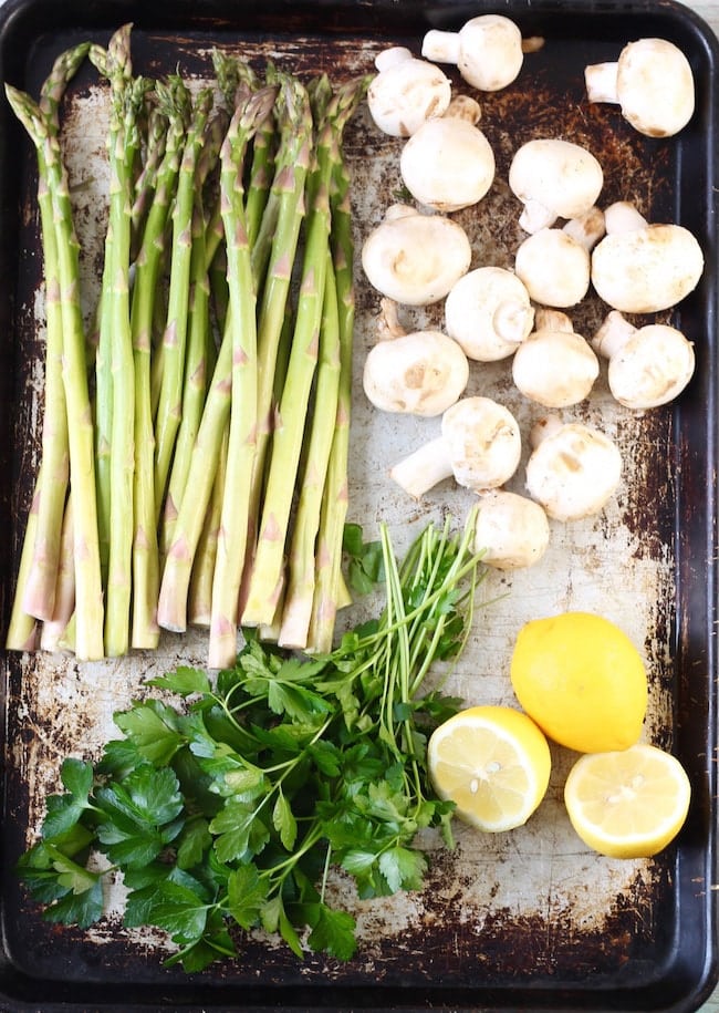 Fresh asparagus, mushrooms, parsley and lemons on a sheet pan