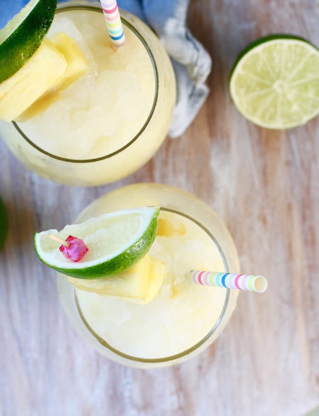 Frozen Pineapple Limeade garnished with lime slices, pineapple chunks and striped paper straws
