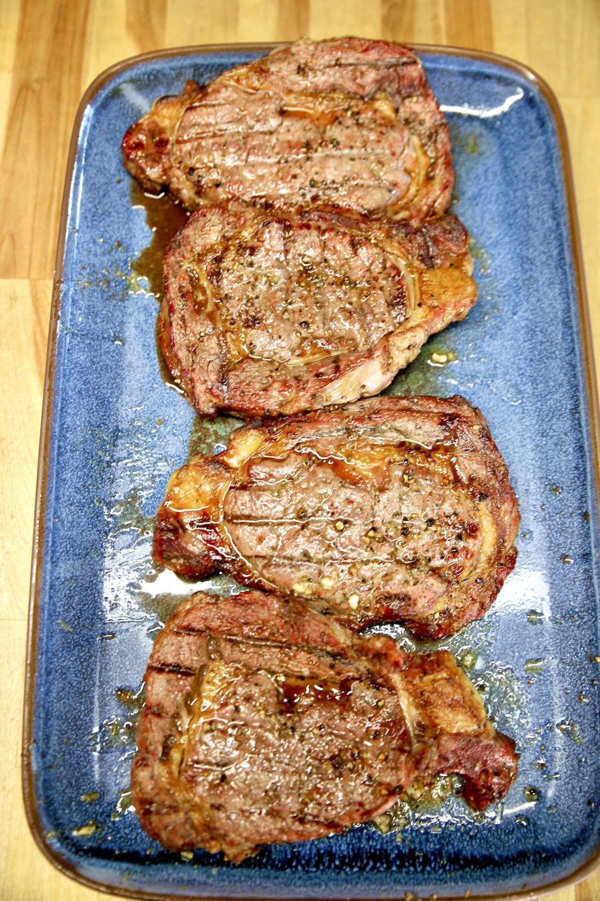 4 Grilled ribeye steaks on a blue platter.