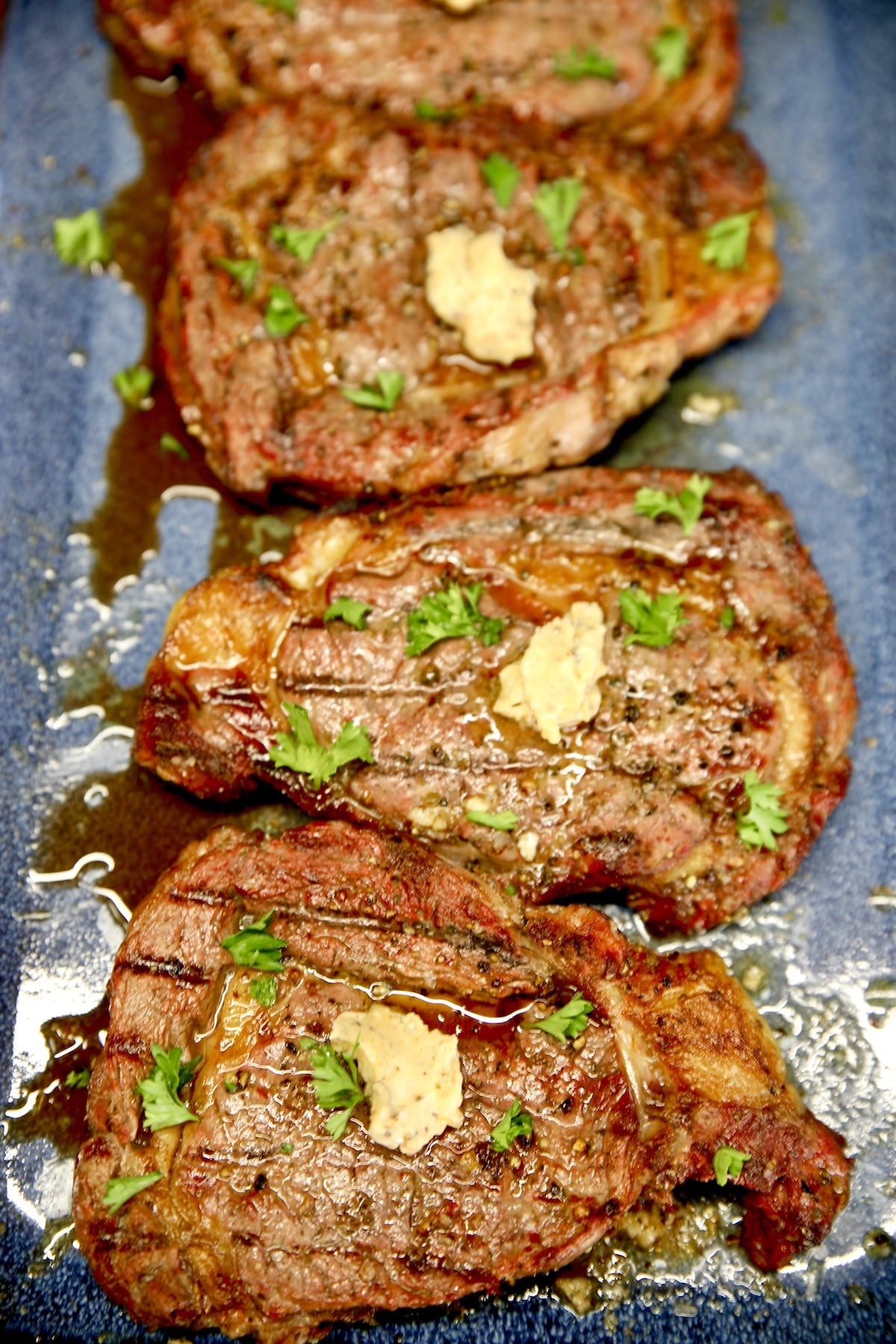 Grilled ribeye steaks with butter on a blue platter.