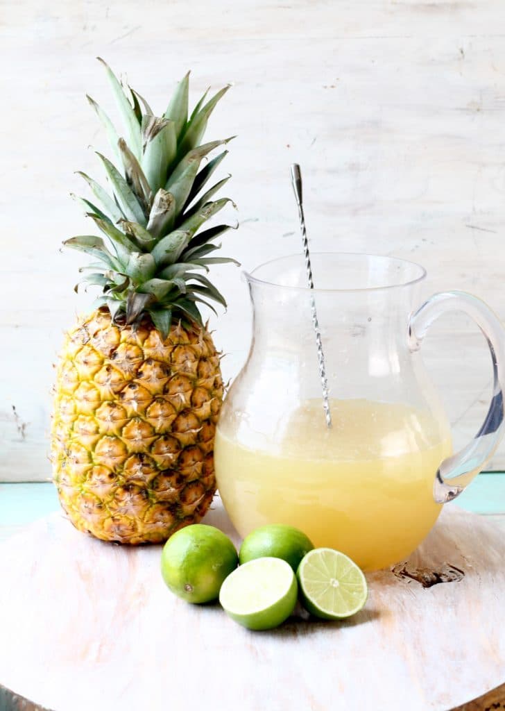 Pineapple Limeade in a pitcher with a fresh pineapple and limes