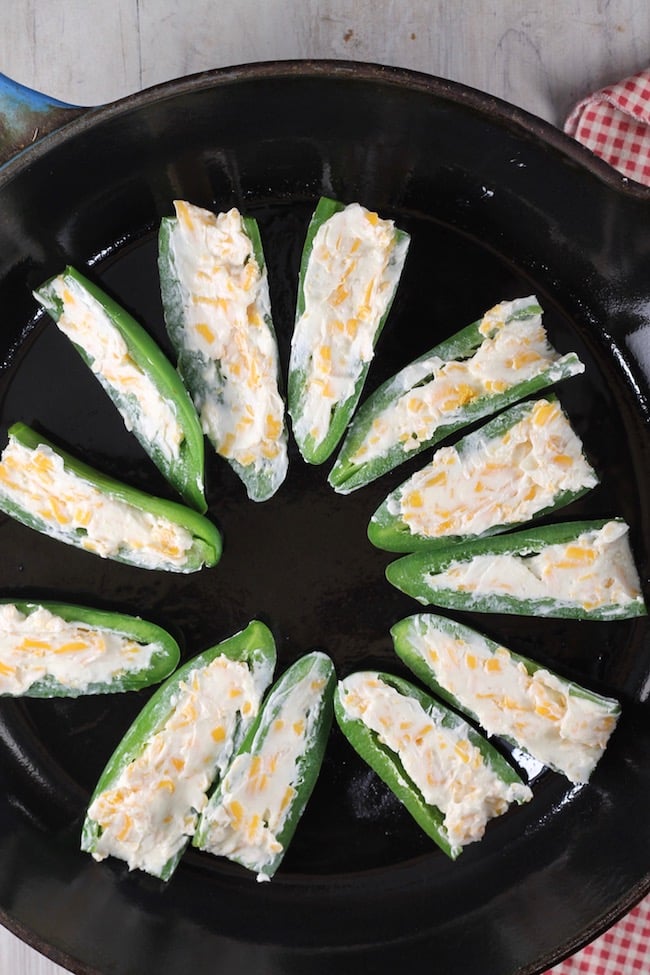 Stuffing jalapeño poppers with cream cheese, garlic and shredded cheddar cheese