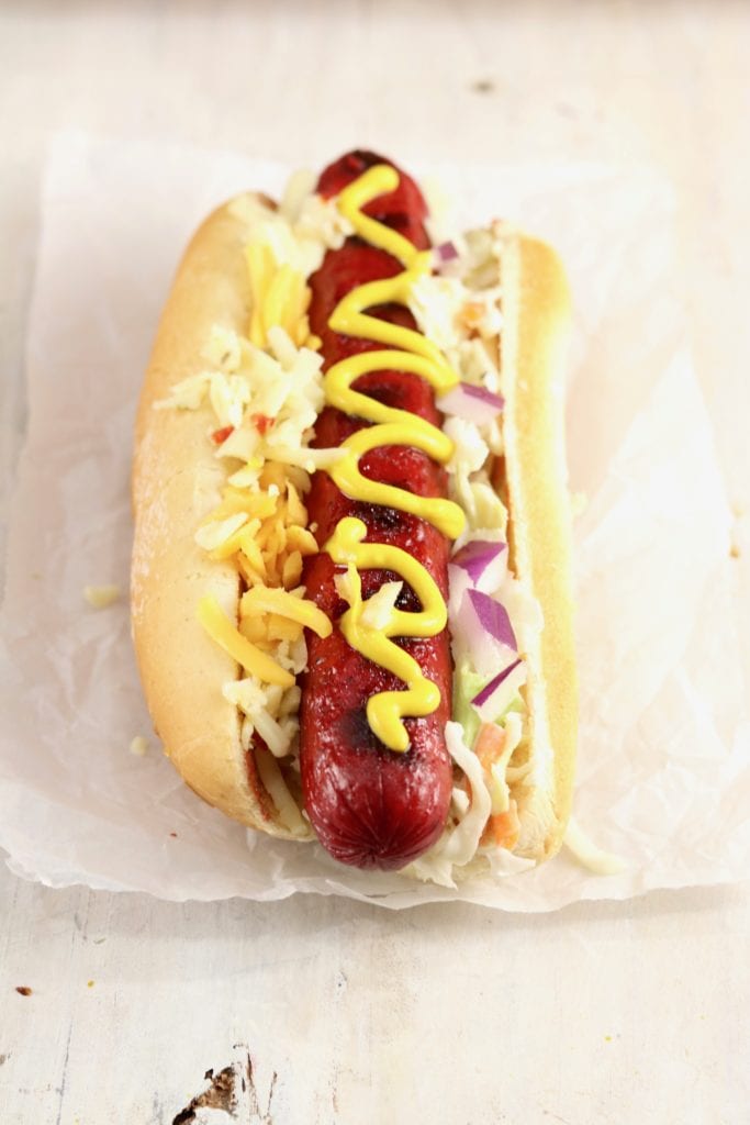 Grilled Hot Dog topped with mustard, slaw, cheese and red onion