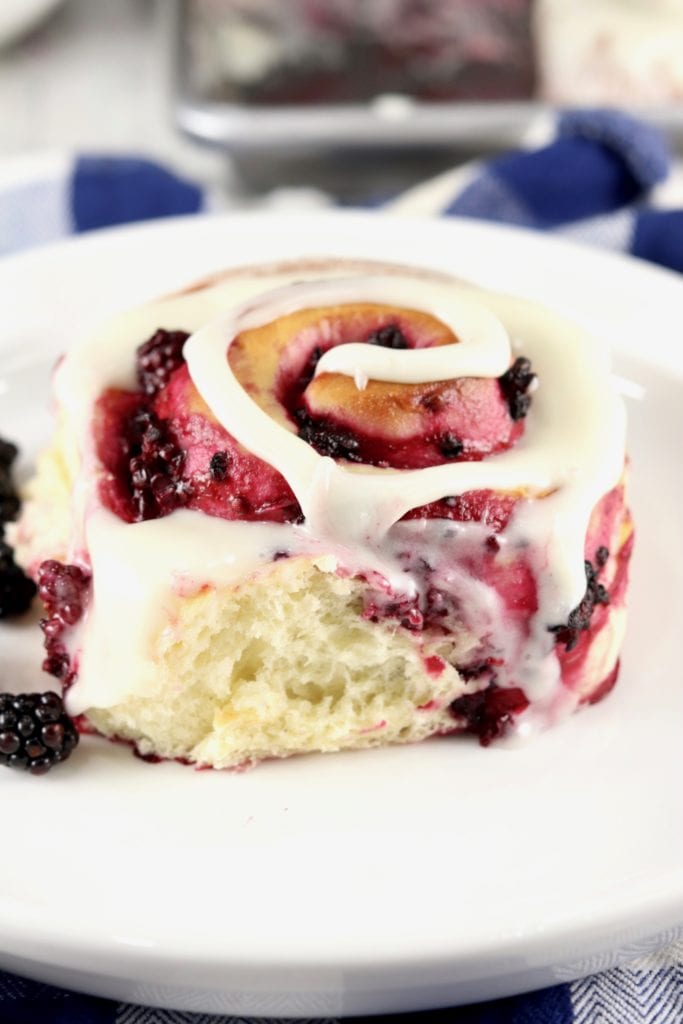 Sweet Roll on a white plate with fresh blackberries. Blue check napkin in background