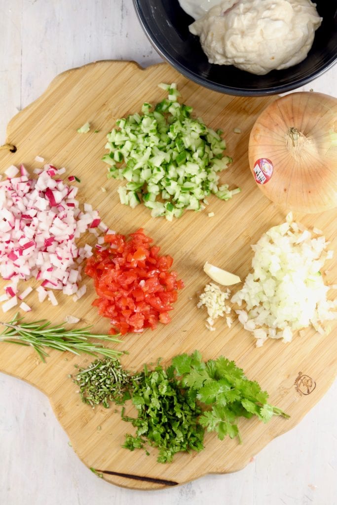 Diced radishes, tomatoes, cucumbers, onions and fresh herbs on a wood cutting board