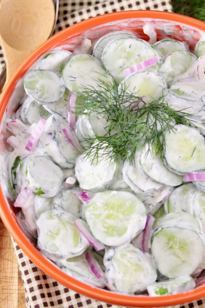 Sliced cucumber salad with creamy dressing and fresh dill in an orange bowl