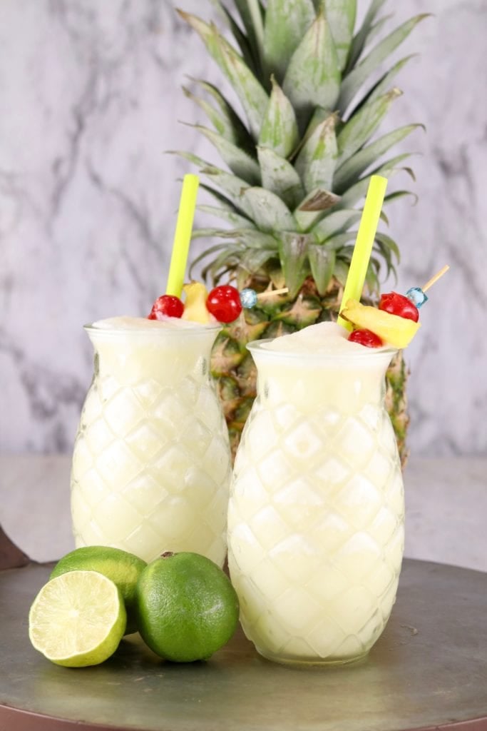Cut glass pineapple glasses filled with pina colada mixture garnished with pineapple and cherries