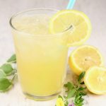 Glass of lemonade with a straw, fresh lemon and greenery beside glass