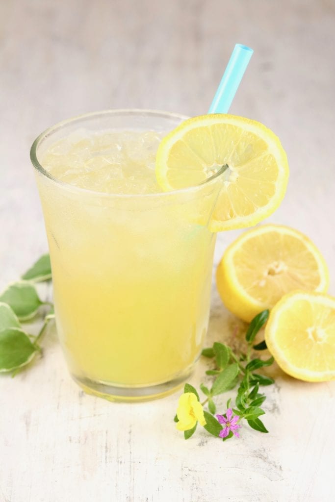 Glass of lemonade with a straw, fresh lemon and greenery beside glass
