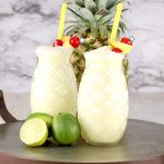 Tray of pineapple glasses with pina colada, fresh line and pineapple in background