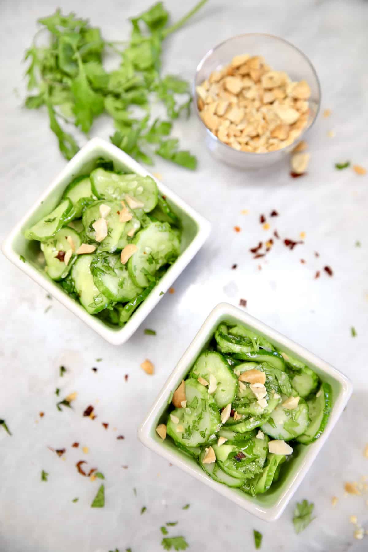 Overhead view of 2 bowls of cucumber salad, small bowl of peanuts.