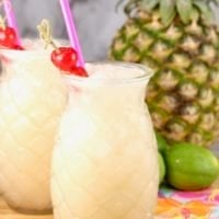 Pineapple Glass with pina colada punch garnished with a cherry and a fresh pineapple and limes in the background
