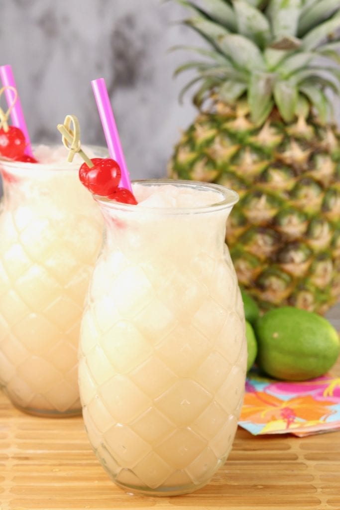 Pineapple Glass with pina colada punch garnished with a cherry and a fresh pineapple and limes in the background