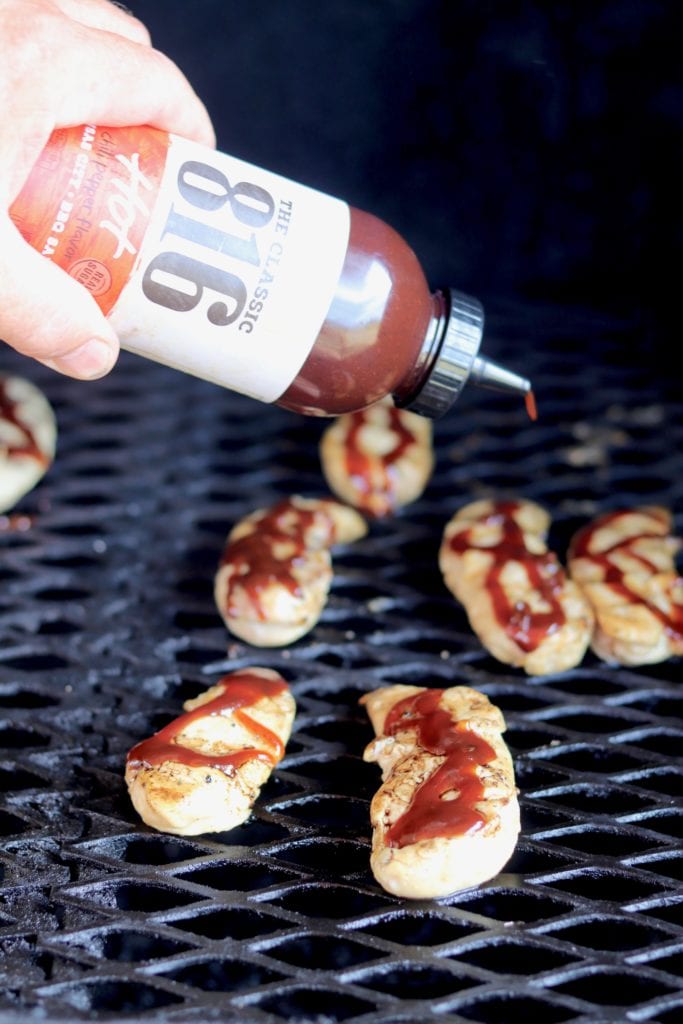 Drizzling grilled chicken tenders on the grill with barbecue sauce