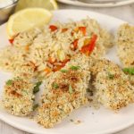 Baked fish sticks on a white plate with rice and fresh lemon slice