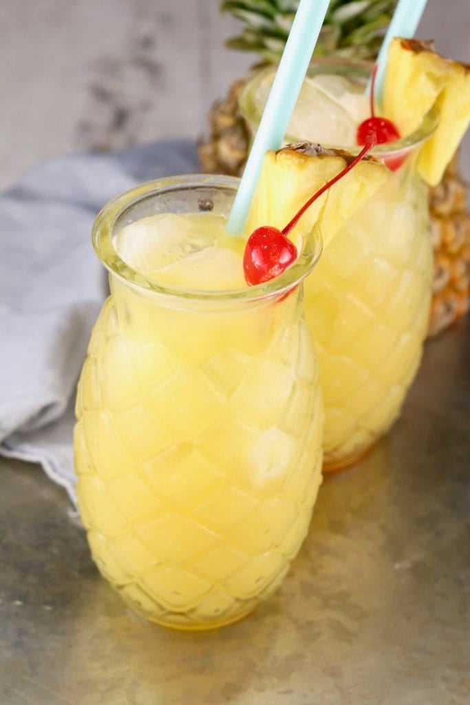 Pineapple drink glasses with cocktails garnished with cherries