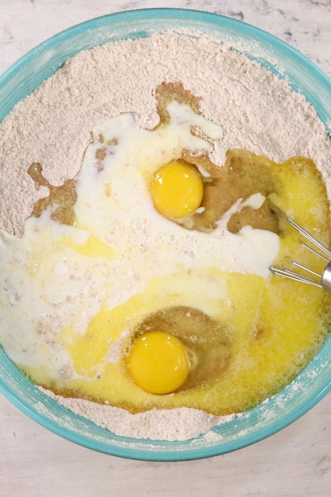 Eggs, milk and melted butter with dry cake ingredients in a blue bowl