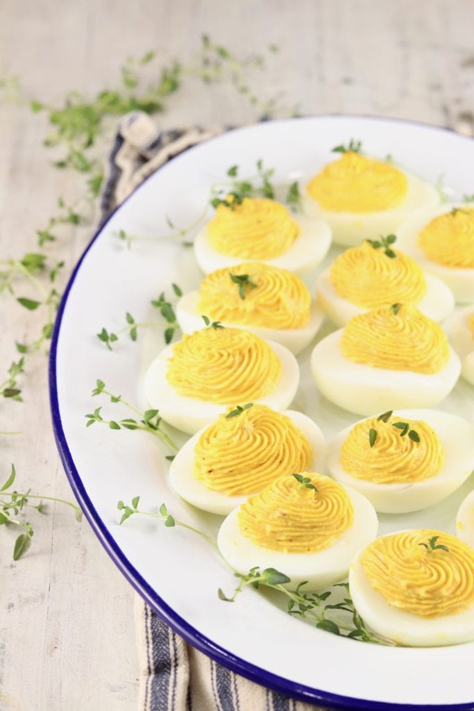 Tray of deviled eggs with thyme garnish