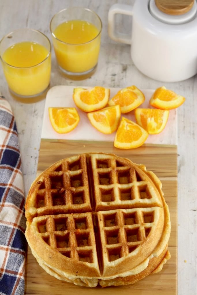 Overhead view of waffles on a board with oranges, orange juice in background