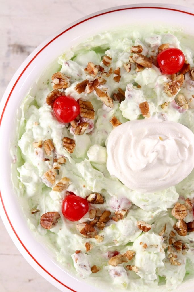 Watergate Salad garnished with cherries and pecansWatergate Salad is a classic potluck and holiday dish that is mixed up in about 5 minutes! Easy pistachio fluff made with crushed pineapple, pecans, cherries and pistachio pudding for a festive dish that anyone can make!