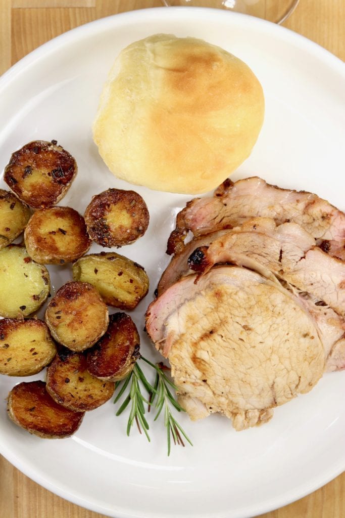 Plate of sliced pork, roasted potatoes and a dinner roll