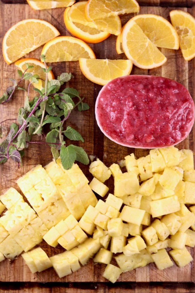 Pineapple Chunks, Pureed Strawberries, fresh mint and orange slices on a cuttin gboard