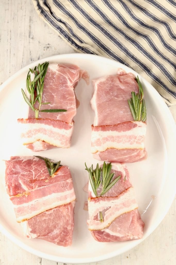 Bacon wrapped pork loin chops with fresh rosemary on a plate - uncooked
