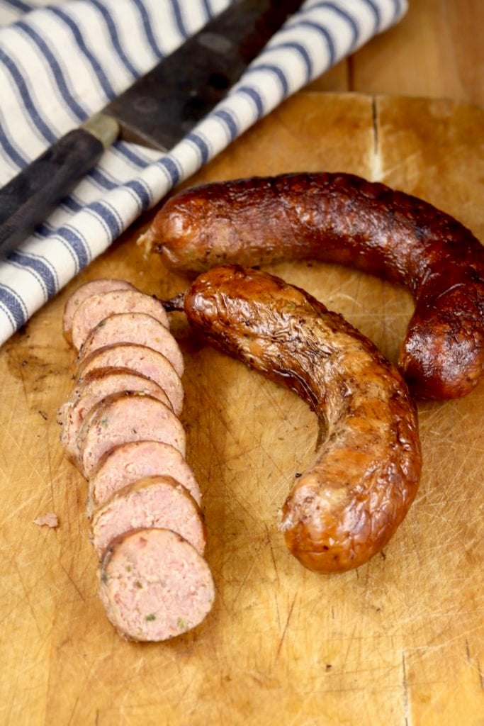 Sliced andouille sausage on a cutting board with knife and 2 unsliced links