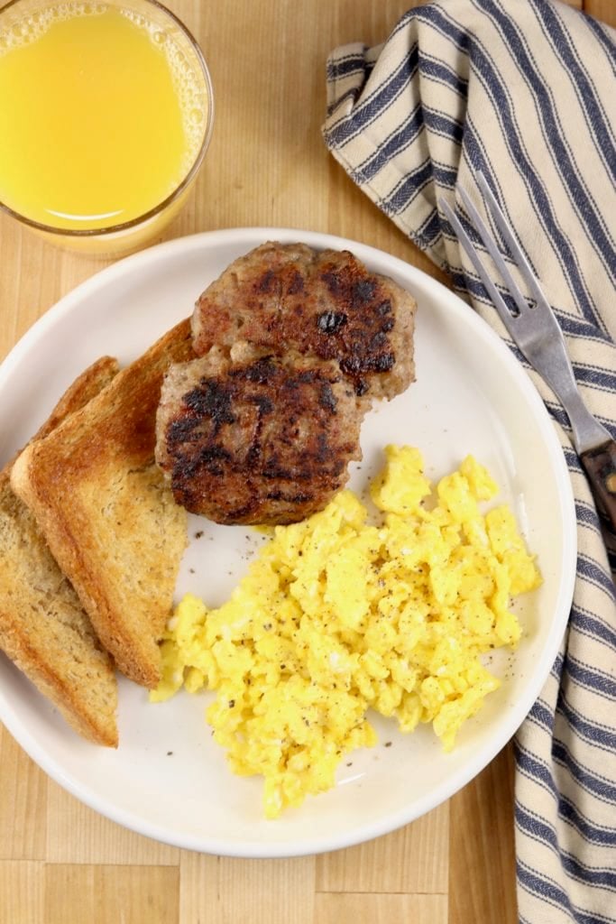 plate of breakfast sausage, scrambled eggs and toast, glass of orange juice