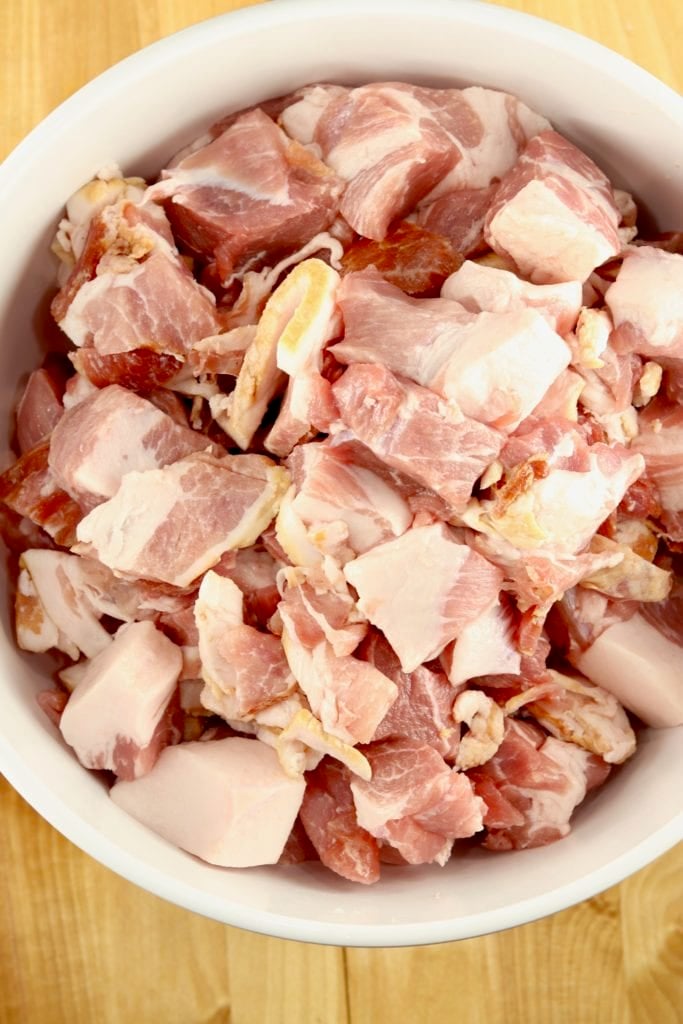 Pork shoulder cut into chunks and mixed with bacon pieces in a bowl