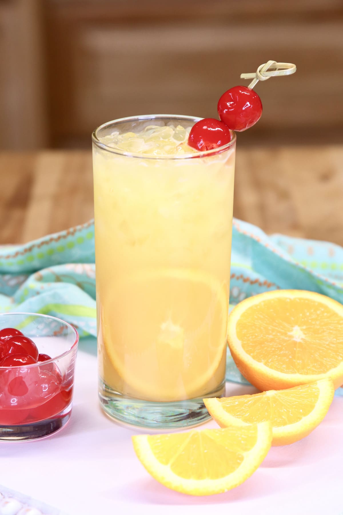 glass of orange juice cocktail with orange and cherry garnishes.