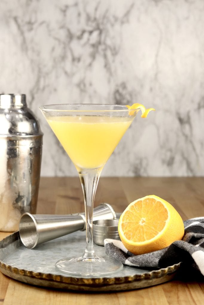Bees Knees Cocktail with a shaker, jigger and sliced orange on a tray