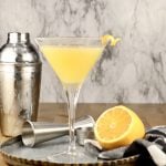 Bees Knees Cocktail in a martini glass with cocktail shaker and a lemon half