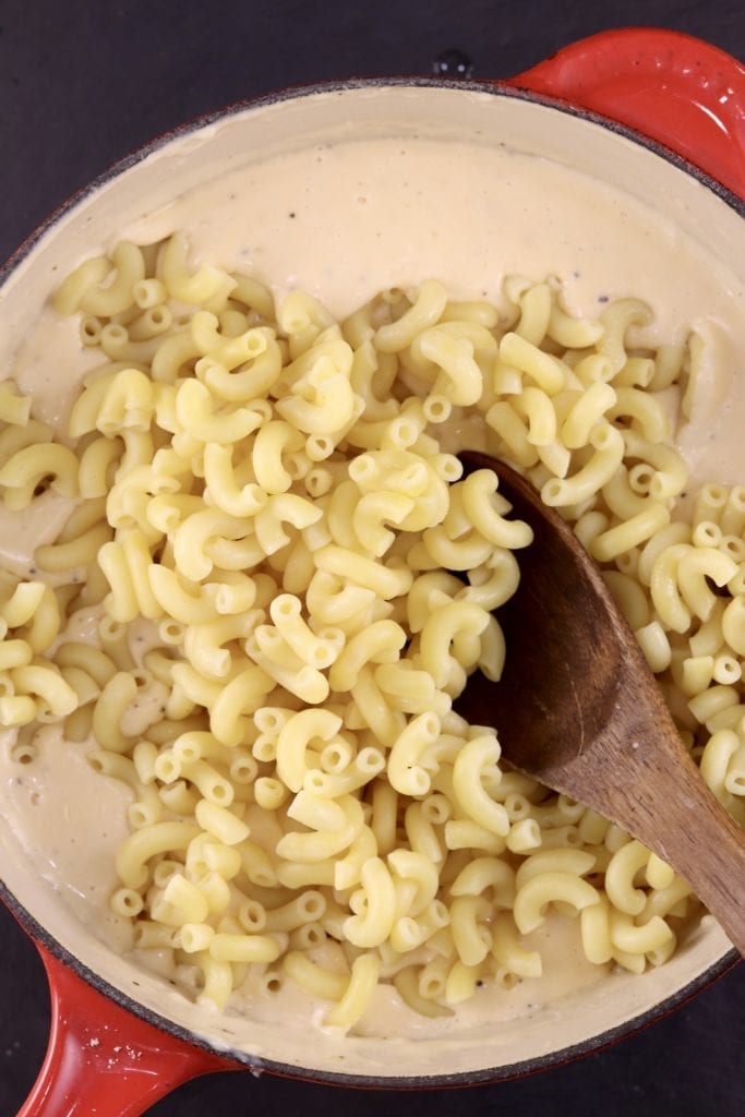Cooked and drained macaroni in a cheese sauce in a pan with wooden spoon