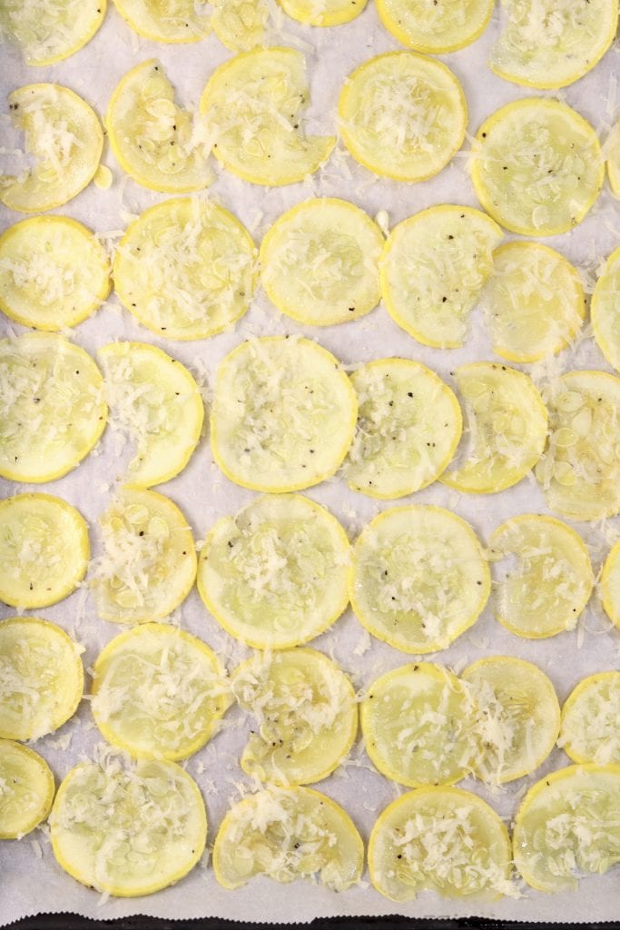 Easy recipe for yellow squash with Parmesan cheese - baked, low-carb side dish Sliced squash sprinkled with Parmesan cheese on a lined baking sheet