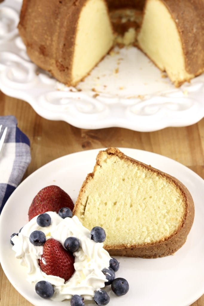 Slice of pound cake with whipped cream and berries, bundt cake in background