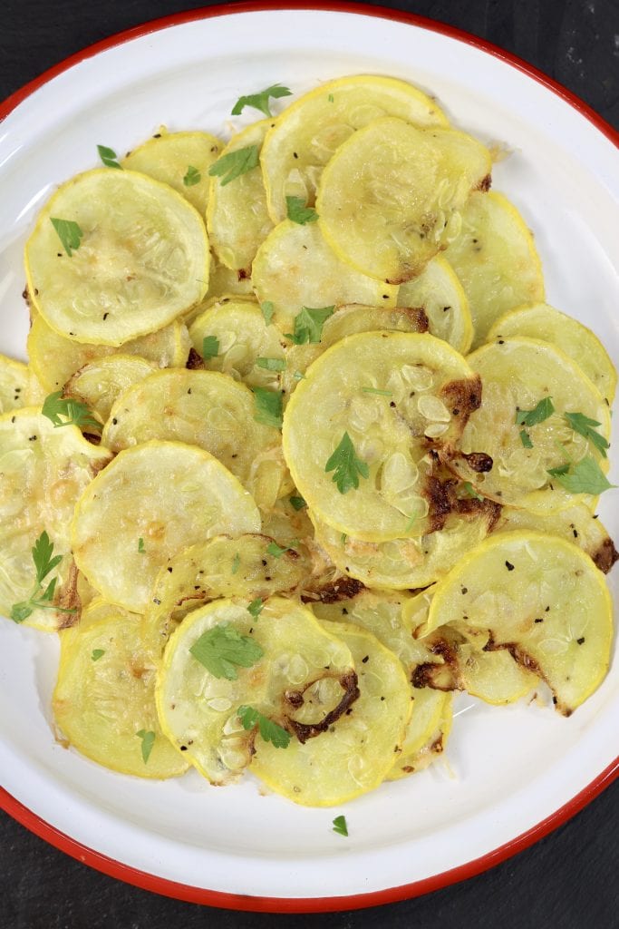 Parmesan Squash is a super simple and delicious side dish to make with yellow squash, Parmesan cheese and a few spices. Baked in the oven for the ultimate low-carb side dish or snack. Sliced yellow squash baked with parmesan cheese, on a white plate