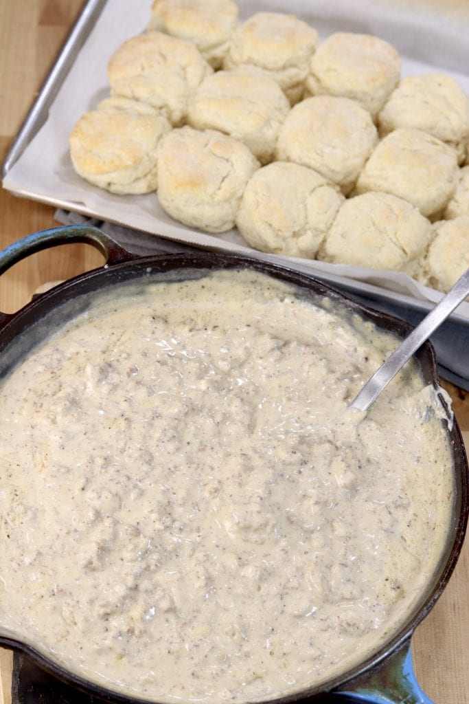 Sausage gravy in a skillet with a pan of buttermilk biscuits