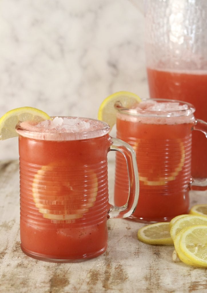 Strawberry lemonade in 2 mugs with pitcher in the background