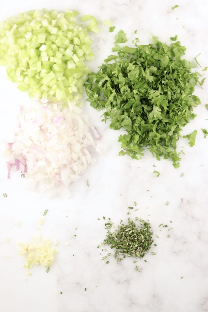 Diced celery, onion, garlic, parsley and rosemary on a light cutting board