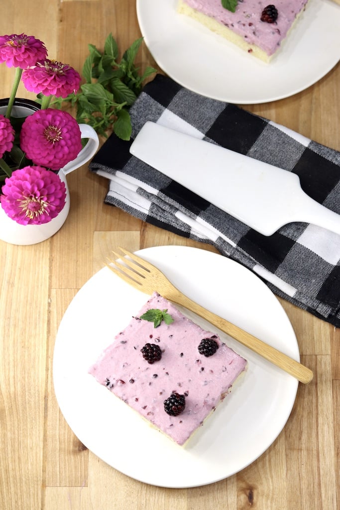 Blackberry Sheet Cake overhead view of a plated slice, pink zinnias in a vase, black and white napkin