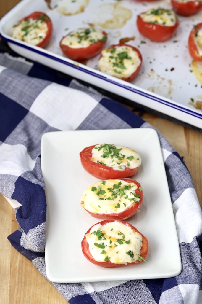 3 cheese stuffed Roma tomatoes on a small plate - baking pan of tomatoes in background