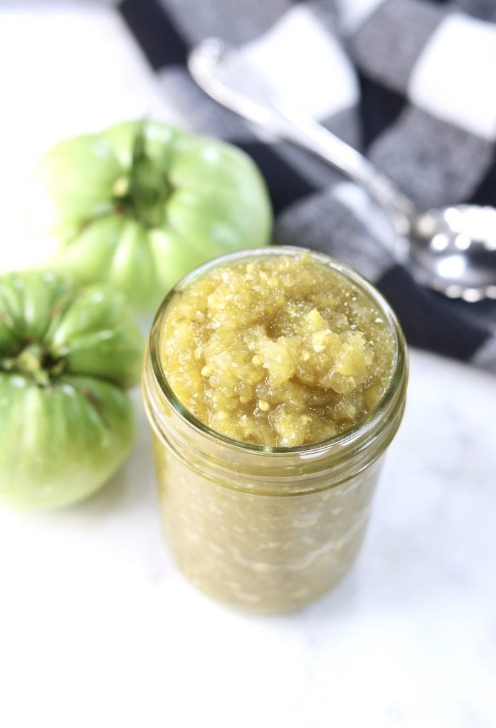Green Tomato Salsa in a jar with 2 green tomatoes and black check napkin