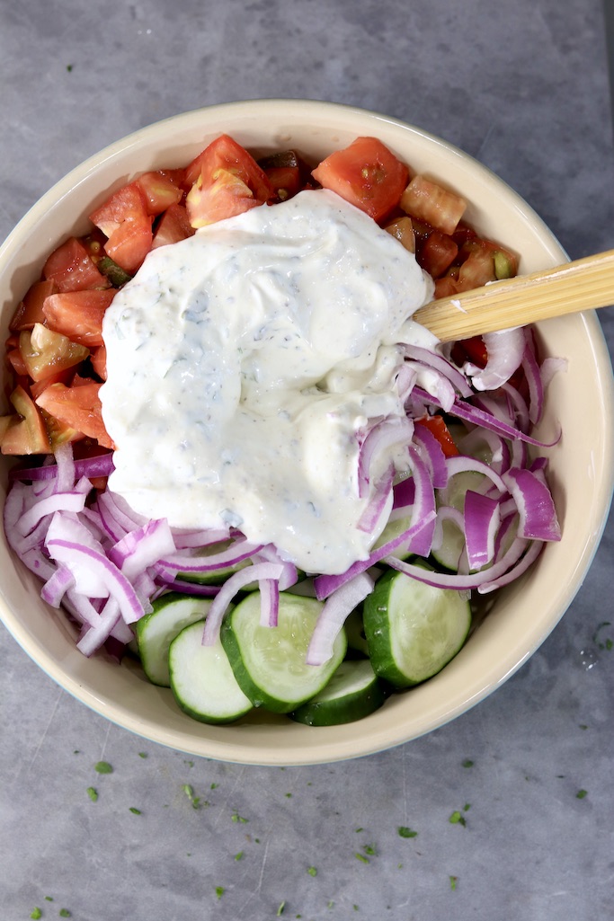 Creamy dressing over chopped tomatoes, cucumbers and onions in a bowl