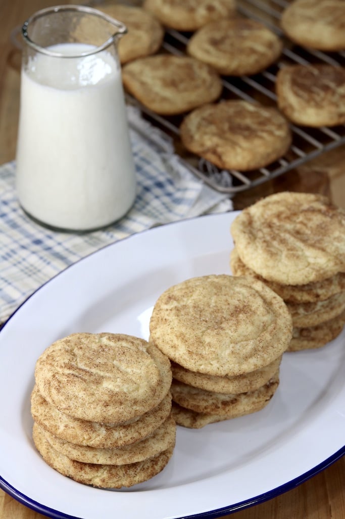 Tray of snickerdoodle cookies with small pitcher of milk behind and a cooling rack of cookies
