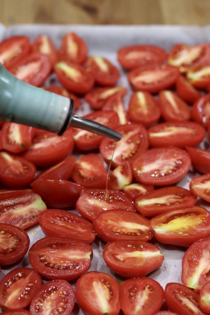 Drizzling olive oil over sheet pan of Roma tomato halves