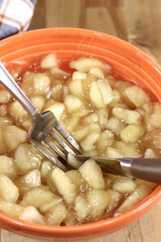 apple pie filling being cut up with a knife and fork in an orange bowl