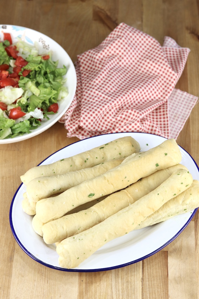 Platter of breadsticks, red napkin with bowl of green salad with tomatoes