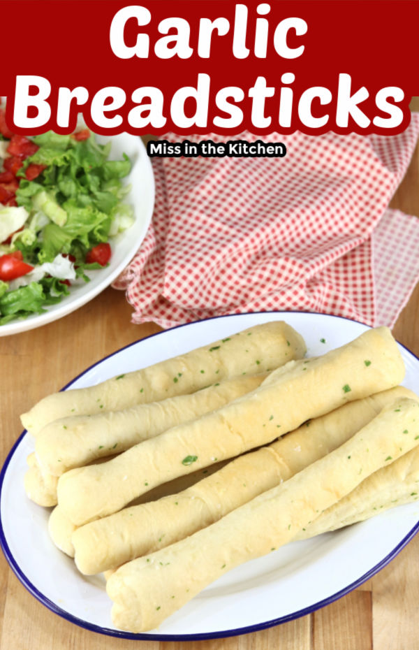 Garlic Breadsticks on a platter - side salad with tomatoes, red napkin - text overlay